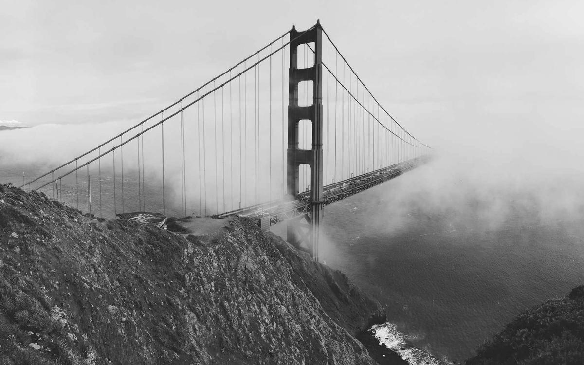 Suspension bridge tower rising through coastal fog above dark cliffs